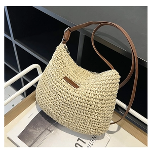 Detail of hand-woven straw texture and brown leather strap on cream half-moon beach bag