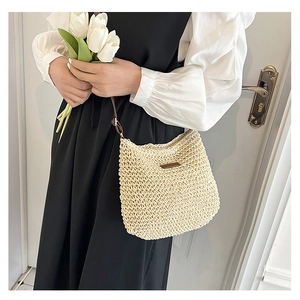 Detail of hand-woven straw crossbody bag with brown leather strap and brand patch