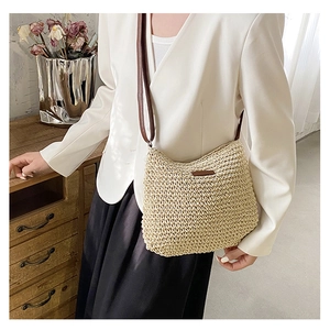 Detail of hand-woven straw crossbody bag with brown leather patch and slim shoulder strap