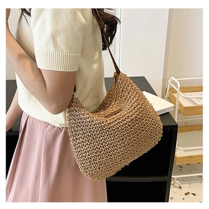 Detail view of woven straw hobo bag with brown leather shoulder strap on a model