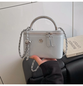 Close-up of a light grey mini square bag with flower-shaped buckle and metal handle