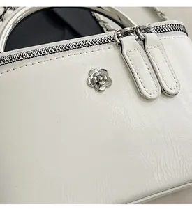 Detail of white glossy mini bag with gold round handle and floral metal logo