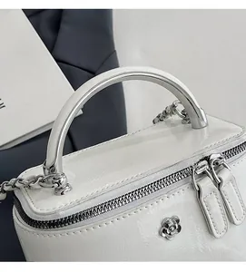 Detail of white patent leather bag featuring silver metal handle and floral clasp