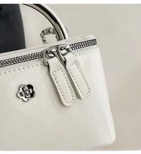 Detail of white patent leather bag with dual zipper and silver camellia flower metal charm