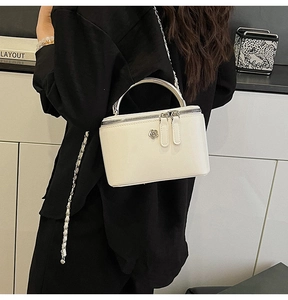 Close-up of white box bag with silver camellia badge and chain leather strap