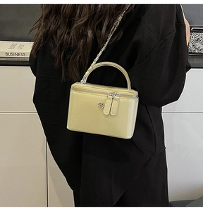 Detail of light yellow mini box bag with chain strap worn crossbody style by a model