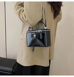 Detail of glossy black patent leather mini box bag with silver flower logo and chain