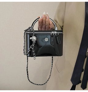 Macro detail of glossy black leather box bag with silver camellia and adjustable chain