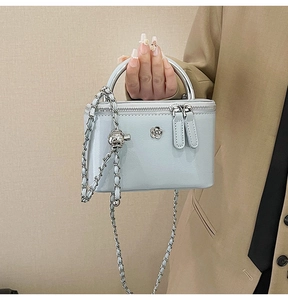 Detail of light blue patent leather mini bag with gold chain strap and floral metal logo