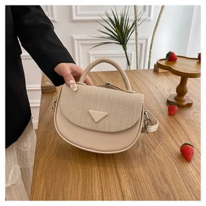 Detail der Klappe mit Flechtstruktur und silberner Dreiecks-Hardware an beiger Tasche
