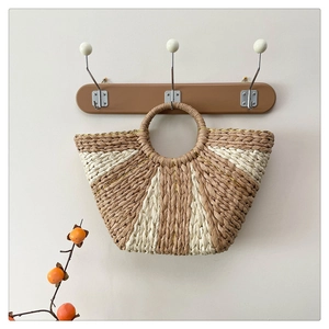 Dettaglio di una borsa a mano in paglia intrecciata beige e kaki su un gancio di legno
