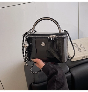 Close-up of black patent leather crossbody bag with silver camellia ornament and chain