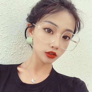 Detail showing oversized clear square glasses frames paired with green stud earrings
