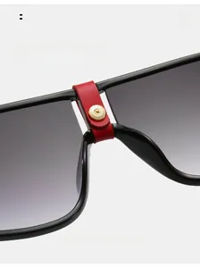 Detail of fashion sunglasses featuring red leather nose bridge and golden screw accent