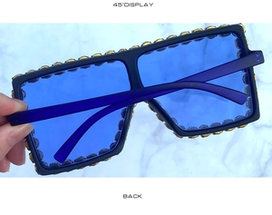 Detail of oversized black square sunglasses with gold floral carvings and blue lenses