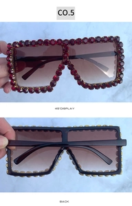 Macro detail of oversized square sunglasses with red rhinestones and gold metal frame