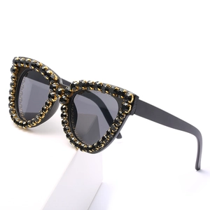 Fashionable cat eye sunglasses with black rhinestones and gold claws on white pedestal