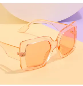 Dettaglio di occhiali da sole squadrati oversize con lenti sfumate arancio-rosa e montatura