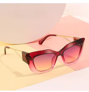 Detail view of cat-eye sunglasses featuring red gradient lenses and golden metal temples