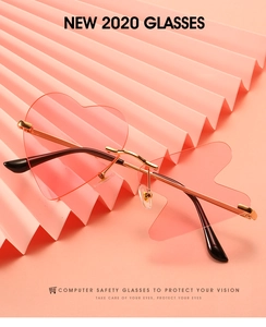 Close-up of heart-shaped rimless pink sunglasses with gold metal frame on a pink backdrop