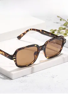 Close-up of tortoise shell square sunglasses on a white marble stand with green plants