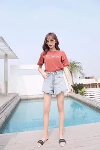 Outdoor shot of brick red short sleeve t-shirt with high waist frayed blue denim shorts