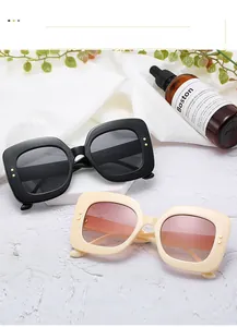 Détail de lunettes de soleil carrées oversize avec rivets dorés sur fond texturé blanc