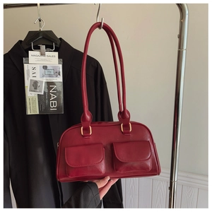 Detail of burgundy faux leather Boston bag with dual front flap pockets and gold hardware