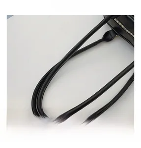 Detail of the reinforced stitching and glossy cylindrical handle on a black leather tote bag