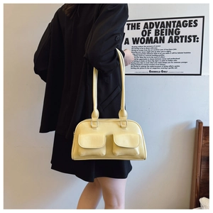 Chic cream-colored bowling bag styled on a shoulder, featuring functional front flap pockets