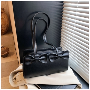 Detail of black faux leather handbag featuring dual bow accents and metal zipper closure