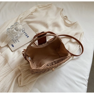 Detailansicht einer Strohtasche mit braunen Ledergriffen auf weißem Kleid drapiert