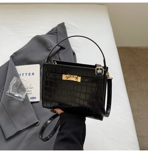 Detail of black crocodile texture bag with gold twist lock on a white surface