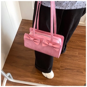 Detail of pink suede handbag featuring dual bow accents and long shoulder straps