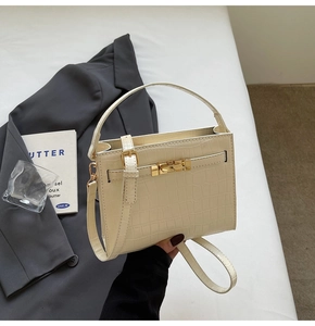 Detailed view of cream crocodile embossed handbag with elegant gold metal lock and handle
