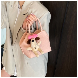 Detail of pink lychee leather handbag featuring a plush dog charm and structured handle
