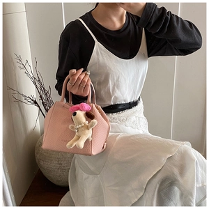 Detail of pink lychee leather handbag with golden logo and cute plush dog charm