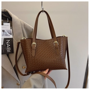 Detail of brown woven leather texture on a shoulder bag with gold metal buckle