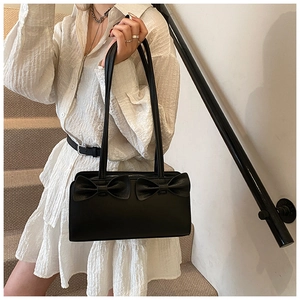 Detail of a chic black leather shoulder bag with decorative bows on a white dress model