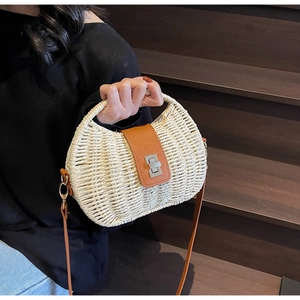 Detail of a beige woven straw bag featuring a brown leather strap and silver metal lock