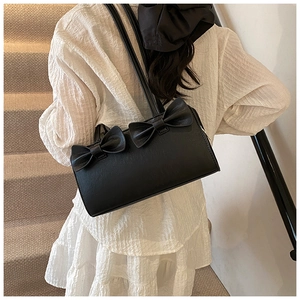 Close-up of a black rectangular bow handbag styled with a white layered ruffle dress