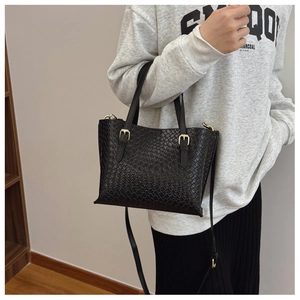 Detail of black woven texture shoulder bag with gold buckles and dual straps shown on model