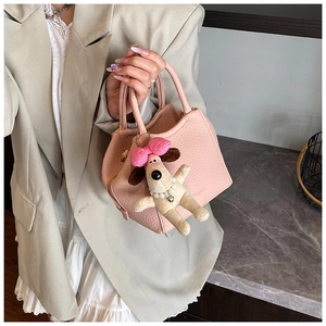 Detail of pink lychee leather handbag with a cute plush dog pendant and bow