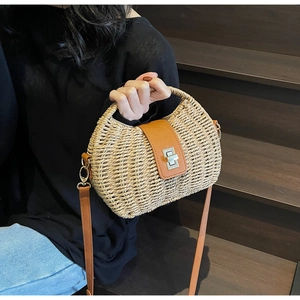 Detail of straw woven crossbody bag with brown leather flap and silver turn-lock clasp