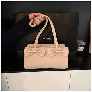 Close-up of beige handbag featuring decorative double bows and matte leather texture
