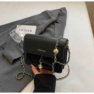Close-up of black crossbody bag with woven texture, golden ball charm, and chain strap
