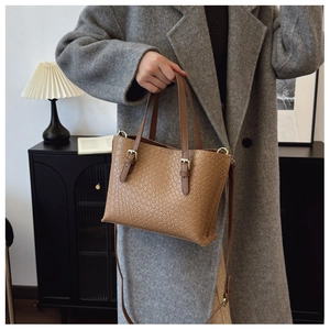 Detail of a brown crocodile texture tote bag with metallic buckles on a wool coat