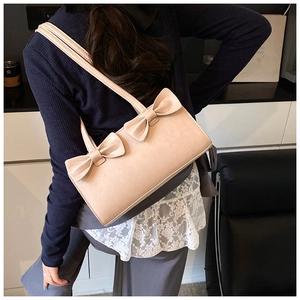 Beige shoulder bag with double bow detail worn by a model in a casual indoor setting