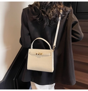 Detail shot of white crocodile embossed handbag with classic metal twist lock and top handle