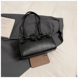 Close-up of black handbag with bows and long strap on a neutral fabric background